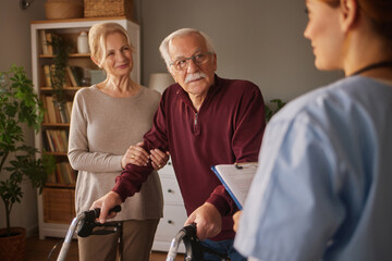 A elderly man with a walker receives medical advice from a professional while being supported by a...