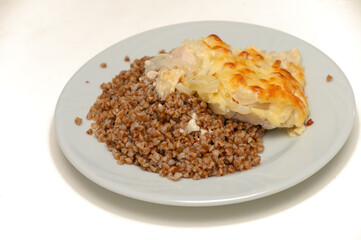 Hearty and wholesome dish of baked meat served with buckwheat porridge on a white plate.