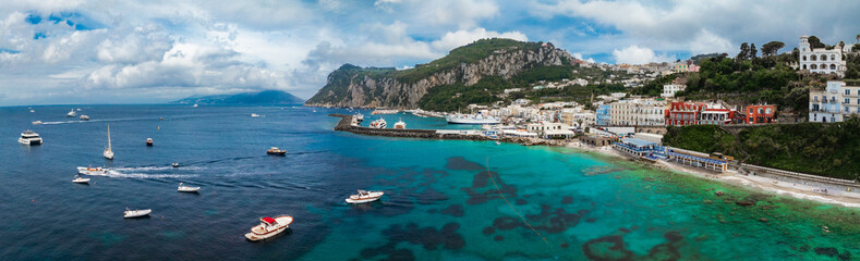 Capri Island's turquoise waters with boats, a rocky cliff with greenery, and a colorful town...