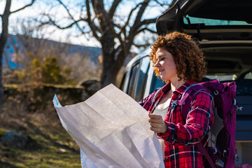 Hiker reading map near car with open trunk in mountain forest