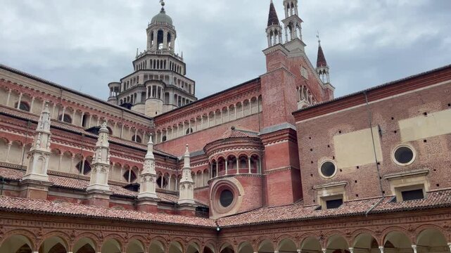 View of the Certosa di Pavia ornate red brick monastery and bell tower from the inner courtyard, showcasing Renaissance and Gothic architectural details under a cloudy sky