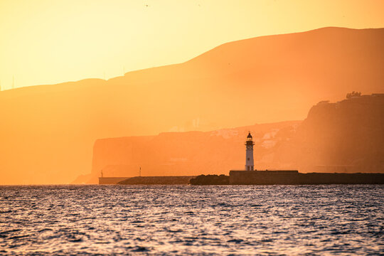 A lighthouse stands against golden coastal cliffs in Almeria