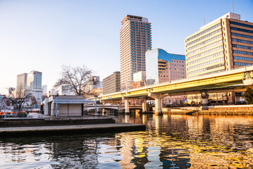 Reflecting golden light on Dojima River at Nakanoshima in Osaka, Japan. A green Island park in the center of Osaka. Highrise building ans bridges