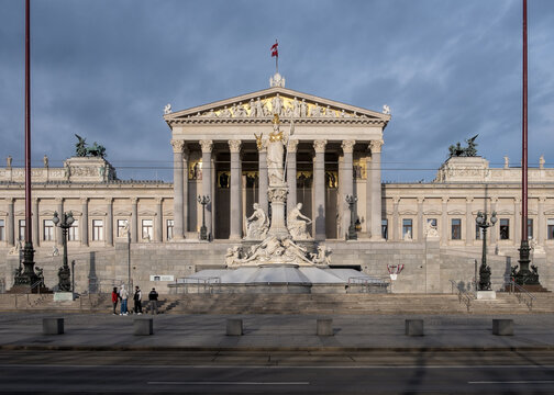 View of the Austrian Parliament's grand neo-Greek entrance facade on Ringstrasse, featuring the monumental Pallas Athena fountain and sculpted ramp of the Theophil Hansen-designed building.