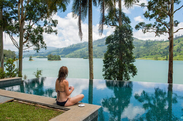 Woman sitting on the edge of the swimming pool of the Summerville Bungalow overlooking the Castlereagh Lake, luxury Ceylon Tea Trails resort, near Hatton, Sri Lanka