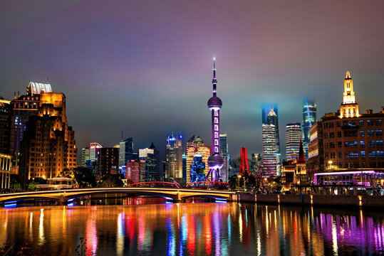 Brightly lit skyline of Lujiazui at night covered in mist viewed from Suzhou Creek in Shanghai, China.