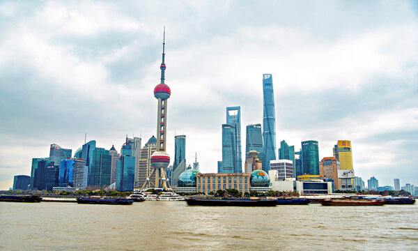 The iconic skyline of Lujiazui along the busy Huangpu River with never ending convoy of cargo vessels, Shanghai, China
