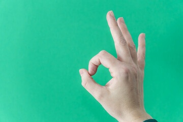 Human hand making okay sign on vibrant green backdrop
