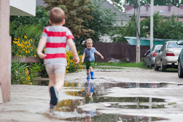 Two Young Children Running Through Rain Puddles in Summer Neighborhood