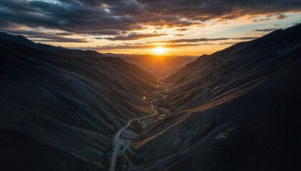Drone surveillance over a remote, rugged mountain pass at sunset. Aerial view of technology monitoring wilderness during golden hour..