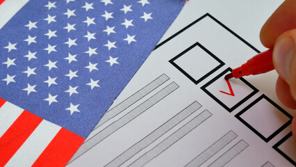 Hand marks box with red marker on ballot. Elections in USA. National flag with stars in background. Transparent voting process allows citizens to actively shape political leadership