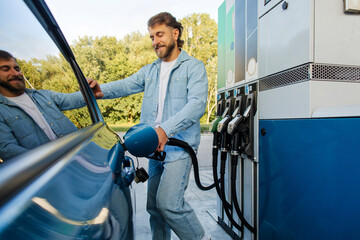 Eco friendly refueling. Man refilling auto with bio fuel at modern petrol station, standing near...