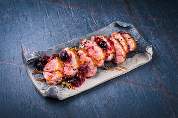 Traditional duck breast roast slices with orange and cranberry sauce served as close-up on a stone...
