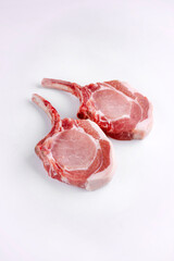 Raw dry aged trimmed bone-in pork loin chops cutlets offered as close-up on white background -...