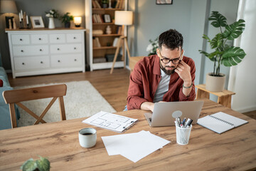 Focused architect working from home on laptop with floor plans
