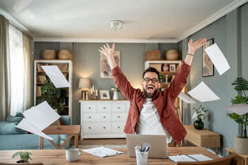Excited freelancer throwing papers in the air celebrating success at home