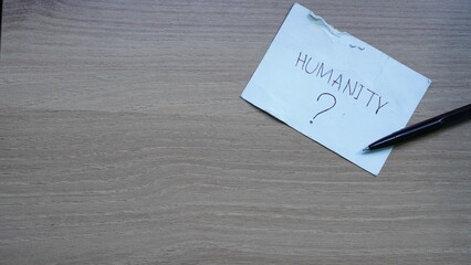 Questioning Humanity: A Torn Note and Pen on Wood