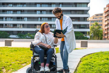 Doctor showing tablet to woman in wheelchair in a park