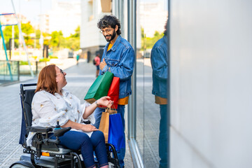 Young man holding shopping bags and talking to woman in wheelchair on city street