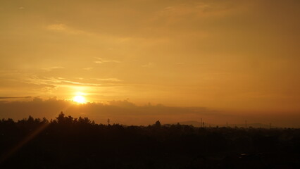 Golden Sunset Over Silhouetted Trees and Distant Structures, Warm Evening Sky