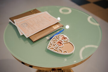 A delicate wooden heart-shaped tray rests on a pastel green circular table alongside a leather...