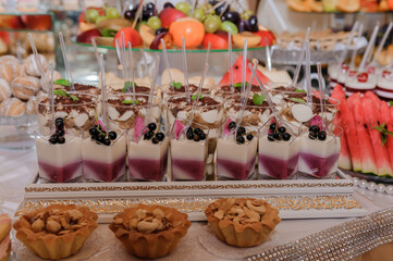 A lavish dessert buffet display featuring rows of berry mousse in glasses, tartlets, fresh fruits, and golden decorative elements on a banquet table setting