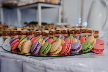 A vibrant display of colorful macarons and layered desserts arranged beautifully on a white-covered table, possibly at a wedding or celebration event
