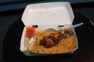Chicken Biryani Takeout Box with Condiments and Plastic Spoon on Dark Surface