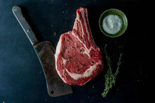 Raw steaks on a metal surface with a meat cleaver, salt and thyme 