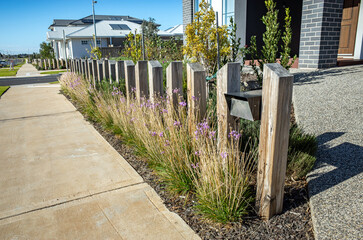 Compact front yard in a suburban neighborhood, featuring vertical timber post fencing, low-maintenance native grasses. Stylish landscaping design for limited urban frontages in modern Australian house