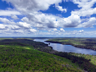 Fototapeta premium Vast, lush forest landscape leading to a large body of water under a dynamic sky filled with white and grey clouds and patches of blue
