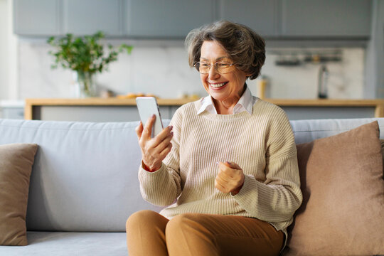 Happy elderly woman using smartphone at home, making video call, consulting doctor at virtual meeting on mobile phone and smiling at screen
