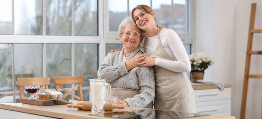 Young woman with her grandmother hugging while baking in kitchen