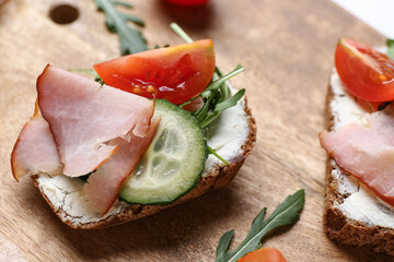 Wooden board of delicious sandwiches with cream cheese, ham and vegetables, closeup