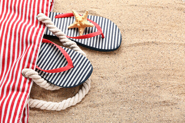Bag with flip-flops and starfish on sand, closeup