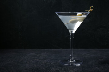 Glass of martini with olives on dark background