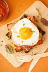 Delicious sandwich with fried egg and bacon on orange background