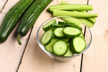 Bowl with fresh cut cucumber on light wooden background
