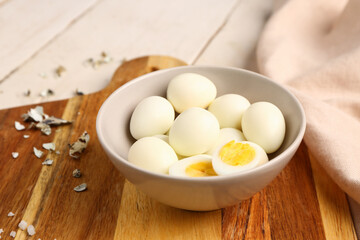 Board with bowl of boiled quail eggs and shells on white wooden background