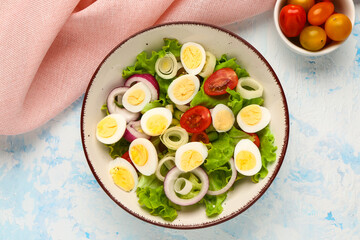 Tasty salad with quail eggs, tomatoes, onion and lettuce on light blue background