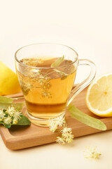 Board with glass cup of linden tea and lemon on beige background