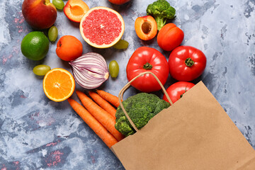Paper bag with different fresh fruits and vegetables on blue background