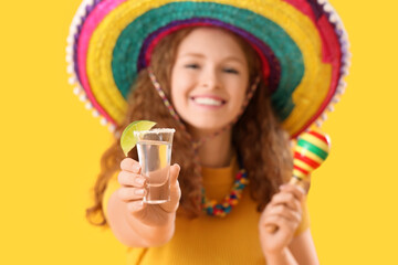 Happy Mexican woman with tequila and maracas on yellow background