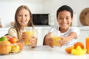 Little children with glasses of fresh citrus juice sitting at table in kitchen