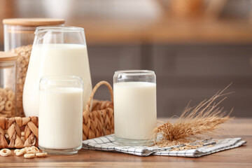 Glasses and jug of fresh milk with cereal rings on wooden table in kitchen