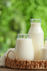 Jug and bottle of fresh milk on wooden table outdoors