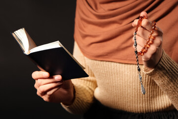 Young Muslim woman with Koran and beads praying on black background, closeup