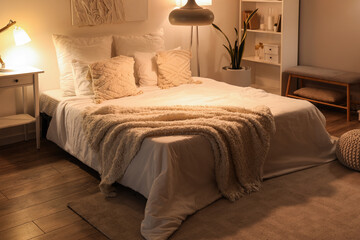 Interior of cozy bedroom with soft blankets on comfortable bed and glowing lamps at night