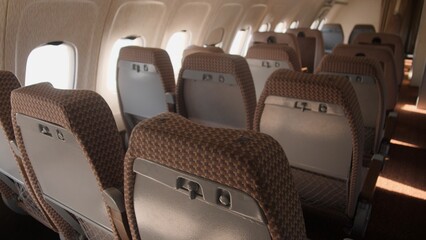 Rows of airplane seats are visible in a cabin with warm lighting, showcasing a quiet and unoccupied space ready for passengers.