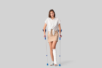 Young woman with broken leg and crutches on light background